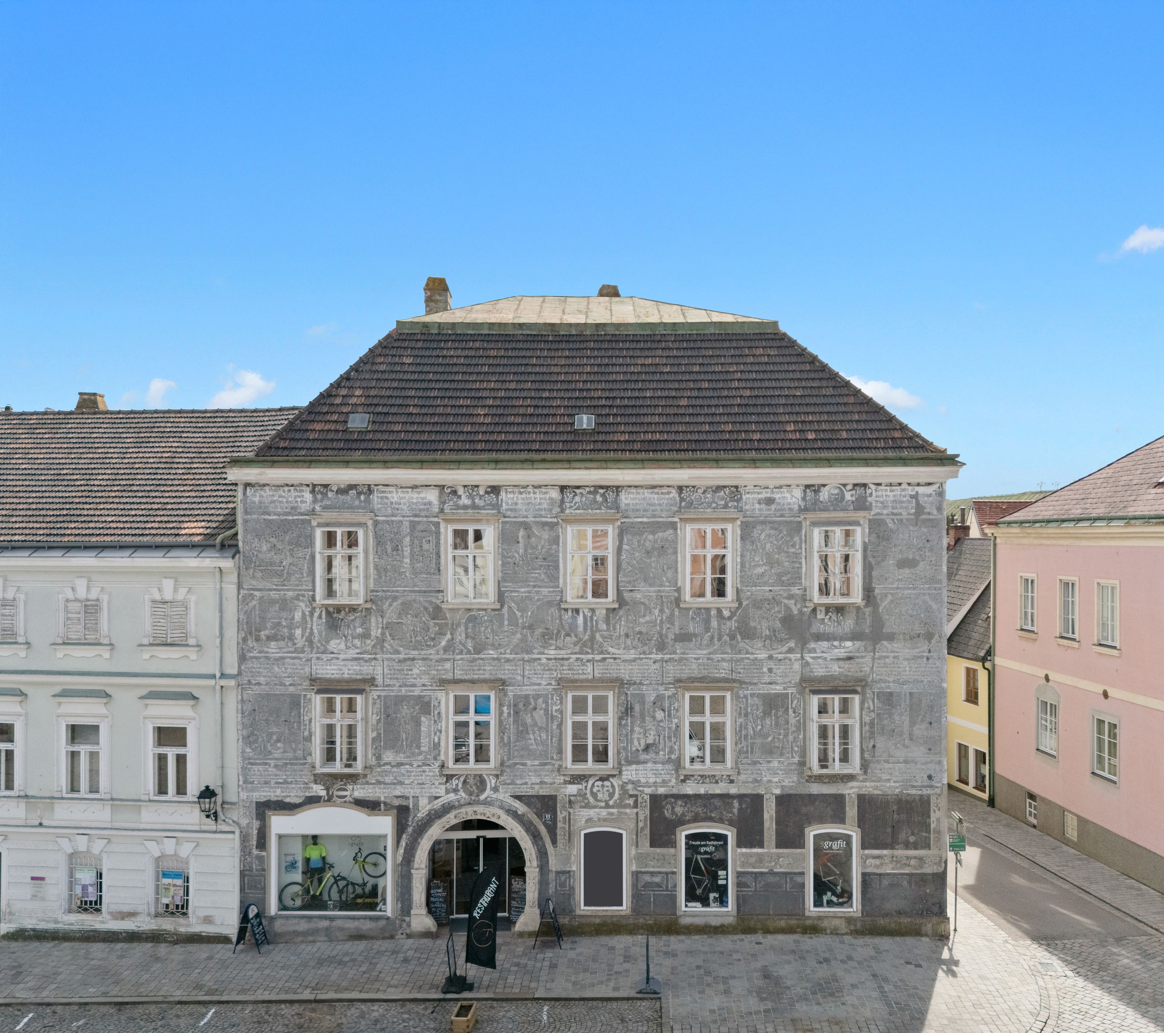 Historisches Gebäude mit grauer Fassade und dekorativen Malereien in einer Stadt.