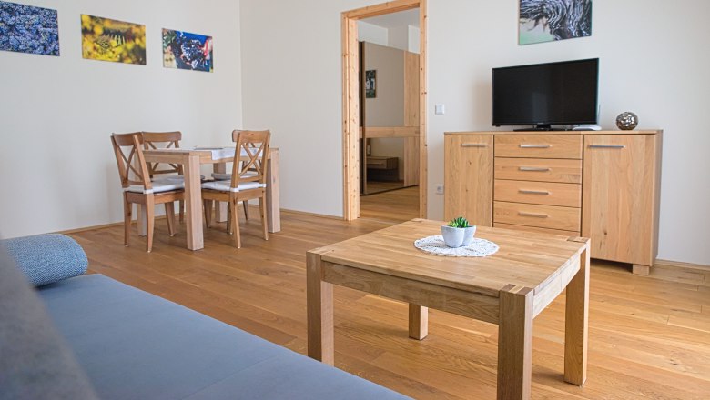 Ein modernes Gästezimmer mit Holzmöbeln, einem Tisch, Stühlen, einem Fernseher und Wandbildern.