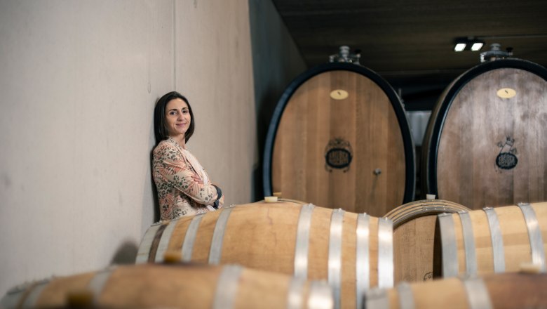 Woman leaning against a wall in a wine cellar with wooden barrels.