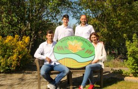 Vier Personen posieren mit einem Schild von 'Bachl's Feldgemüse' in einem Garten.