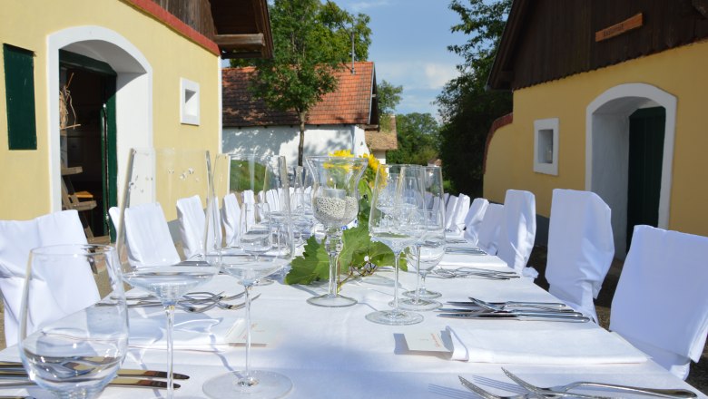 Langer, festlich gedeckter Tisch im Freien mit weißen Tischdecken und Stühlen, umgeben von gelben Gebäuden.