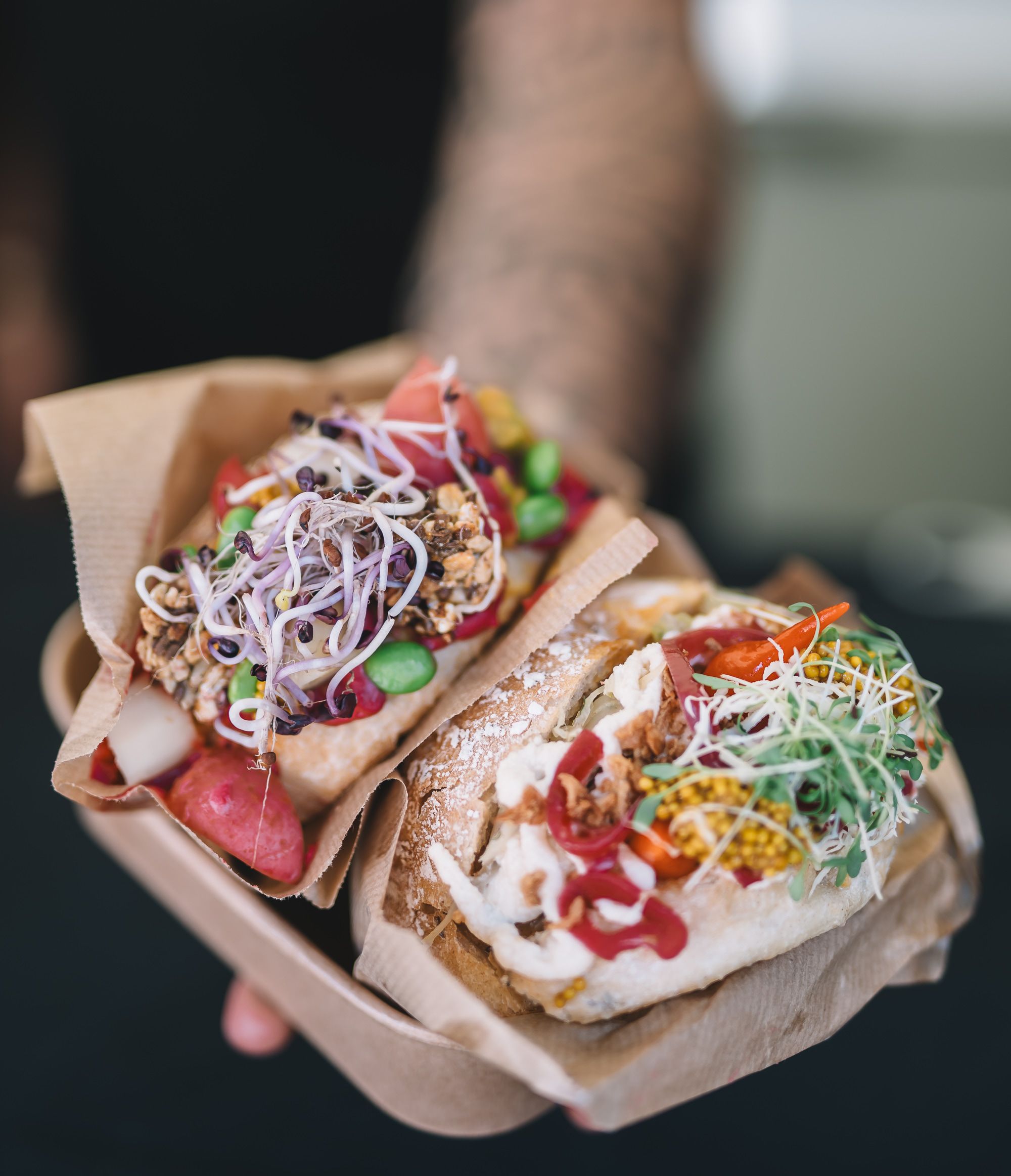 Eine Person hält zwei Winzerweckerl, gefüllt mit regionalen Produkten wie frischem Gemüse, Sauerkraut und mehr, in die Kamera. 