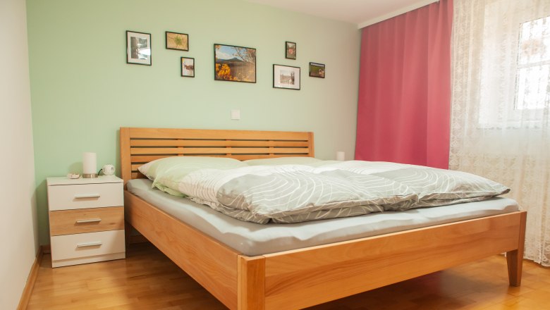 Ein Schlafzimmer mit einem Holzbett, grüner Wand, Bildern, Nachttisch und rosa Vorhängen.