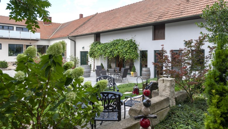 Ein gem&uuml;tlicher Innenhof eines Winzerhofs mit Pflanzen, Gartenm&ouml;beln und Weinf&auml;ssern.