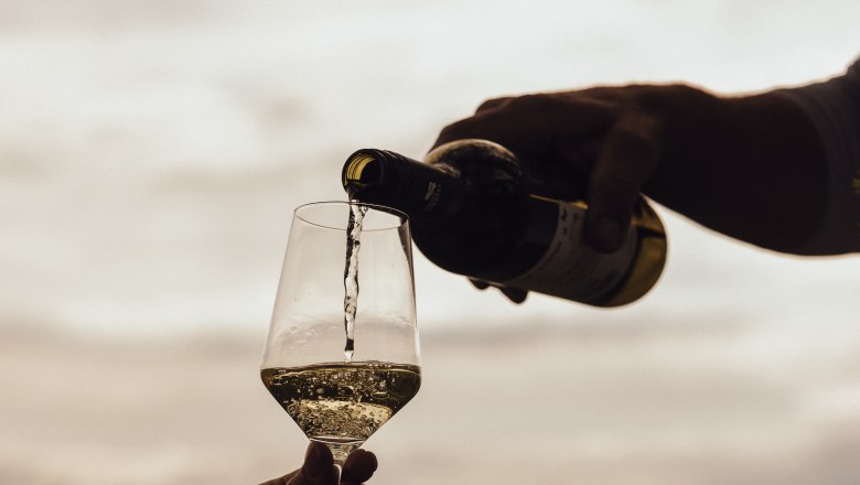 Wine is poured into a glass outdoors, with a landscape in the background.