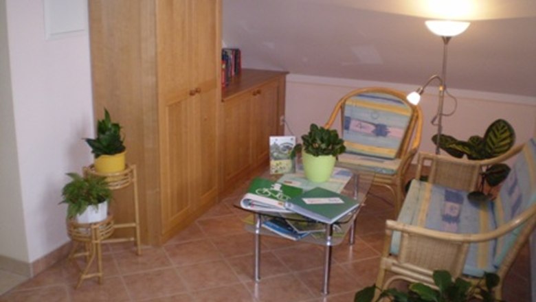 Gemütliche Leseecke mit Rattanmöbeln, Pflanzen und einem kleinen Tisch mit Büchern.