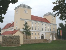 Schloss Wolkersdorf mit zwei Türmen und einem runden Steinturm im Vordergrund.