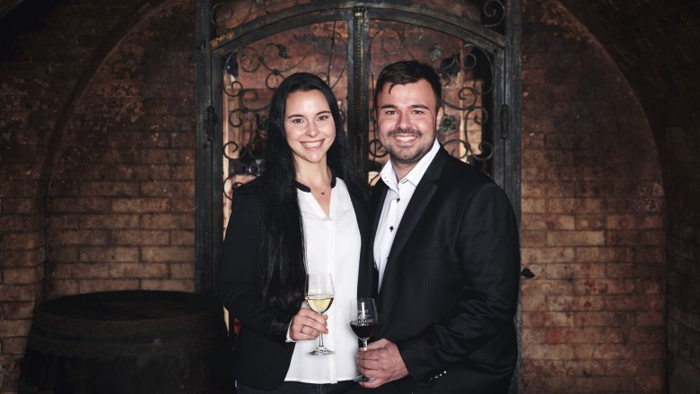 Ein Mann und eine Frau in eleganter Kleidung halten Weingl&auml;ser in einem Weinkeller.