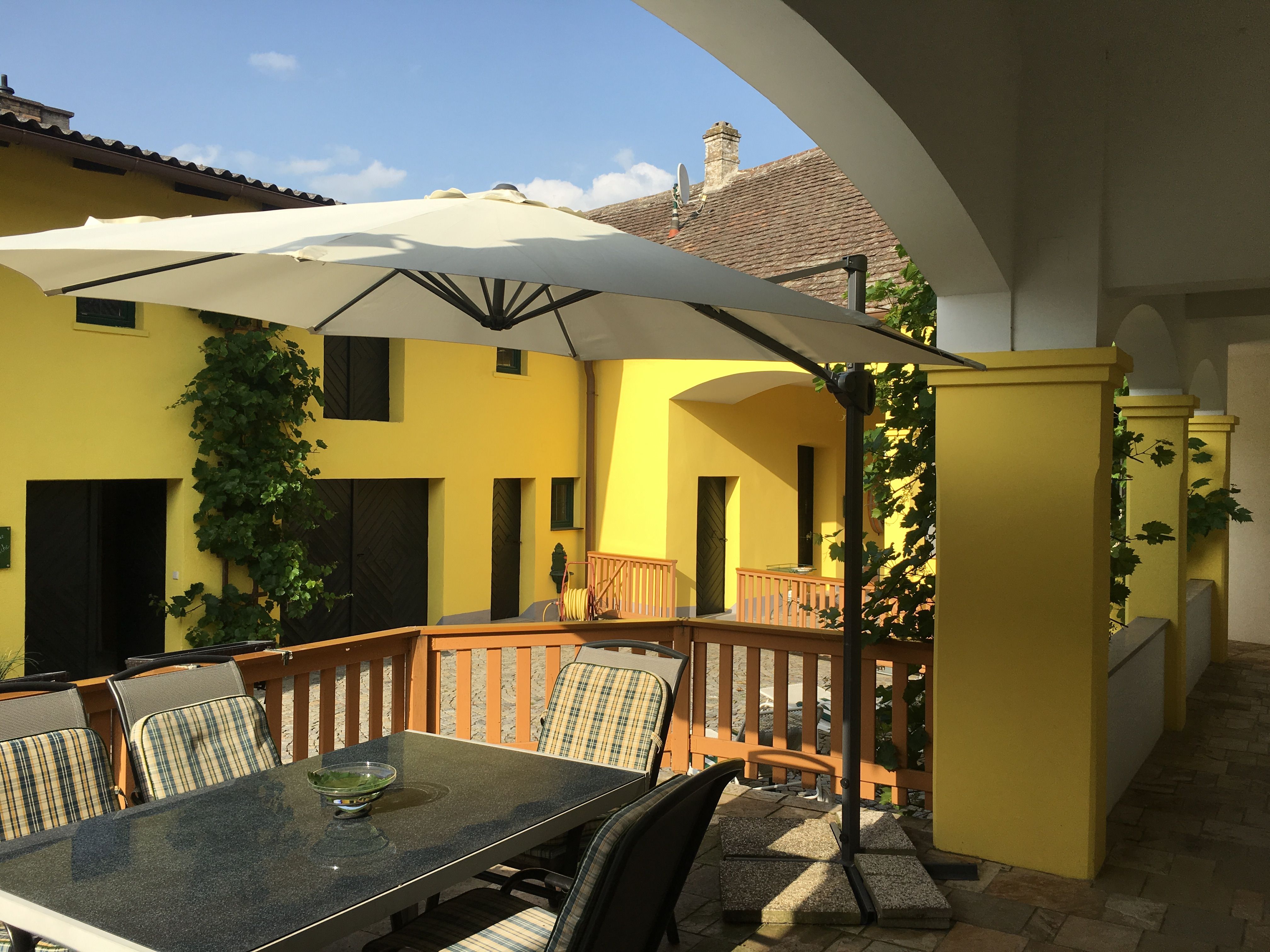 Terrasse mit Tisch, Stühlen und Sonnenschirm vor gelbem Gebäude.