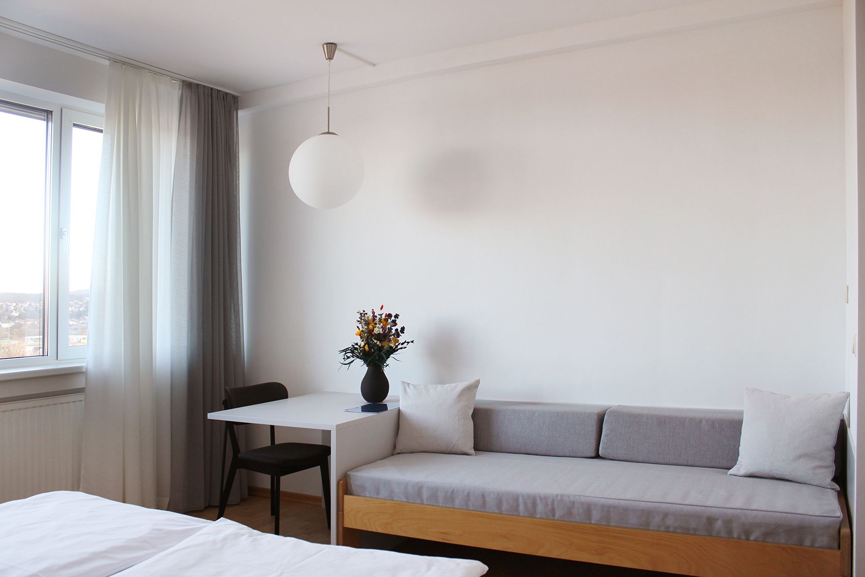 Modernes Gästezimmer mit Sofa, Tisch, Stuhl und Fenster mit Vorhängen.