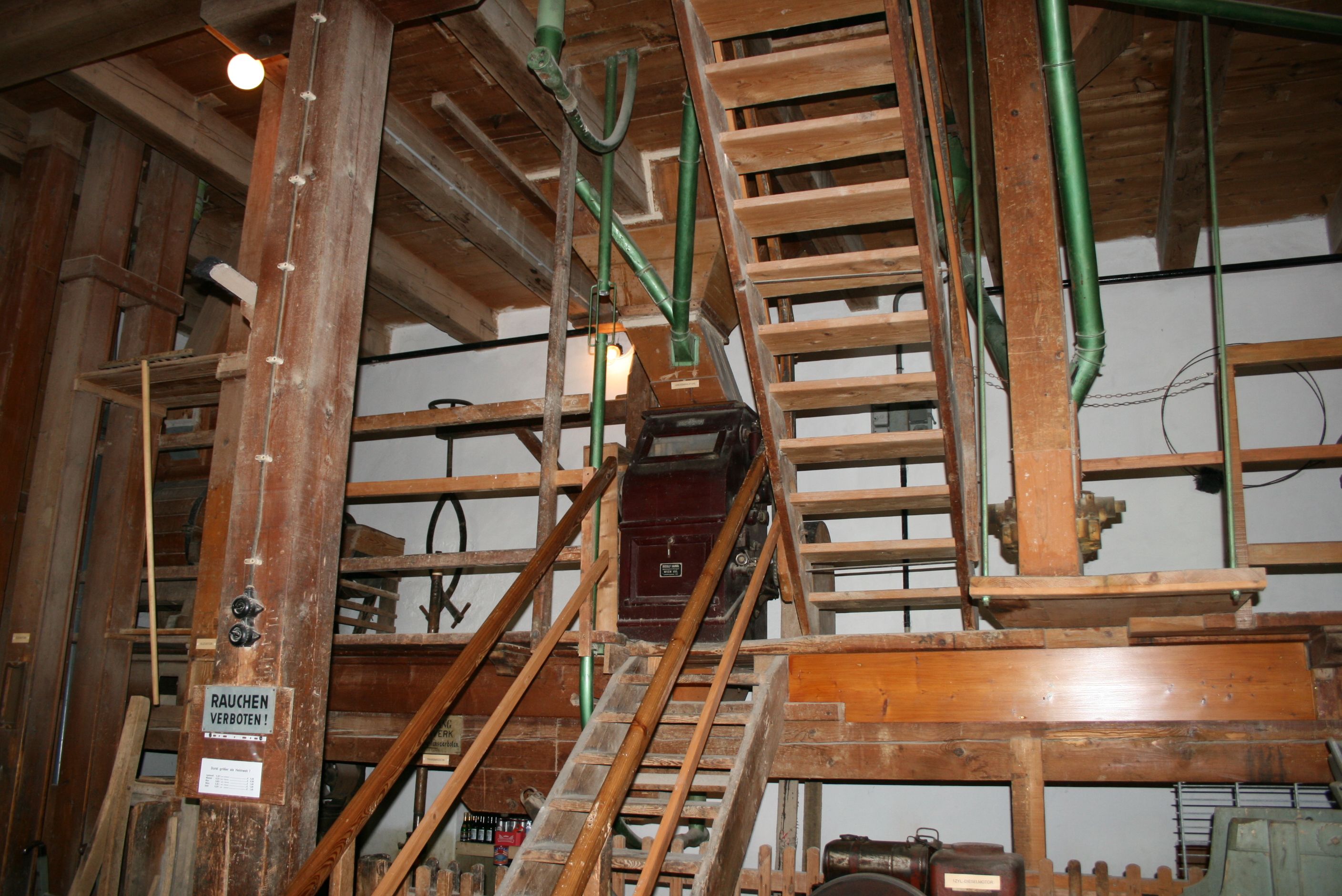 Innenansicht einer alten Mühle mit Holztreppen und Maschinen.