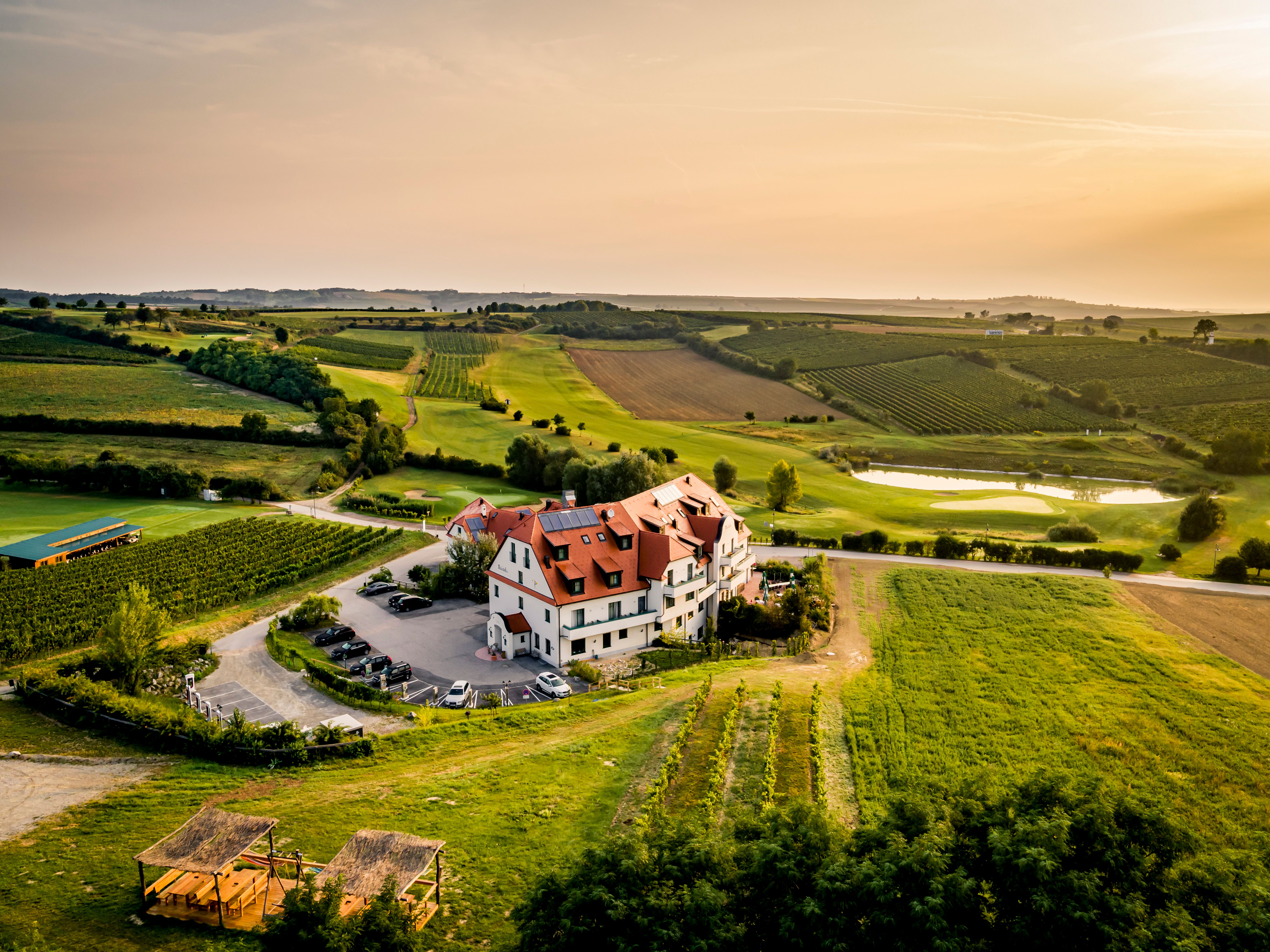 Luftaufnahme eines Hotels inmitten von Weinbergen und Feldern bei Sonnenuntergang.