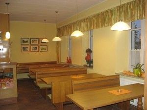 Innenansicht eines gemütlichen Cafés mit Holztischen und Bänken, dekoriert mit Bildern und Pflanzen.