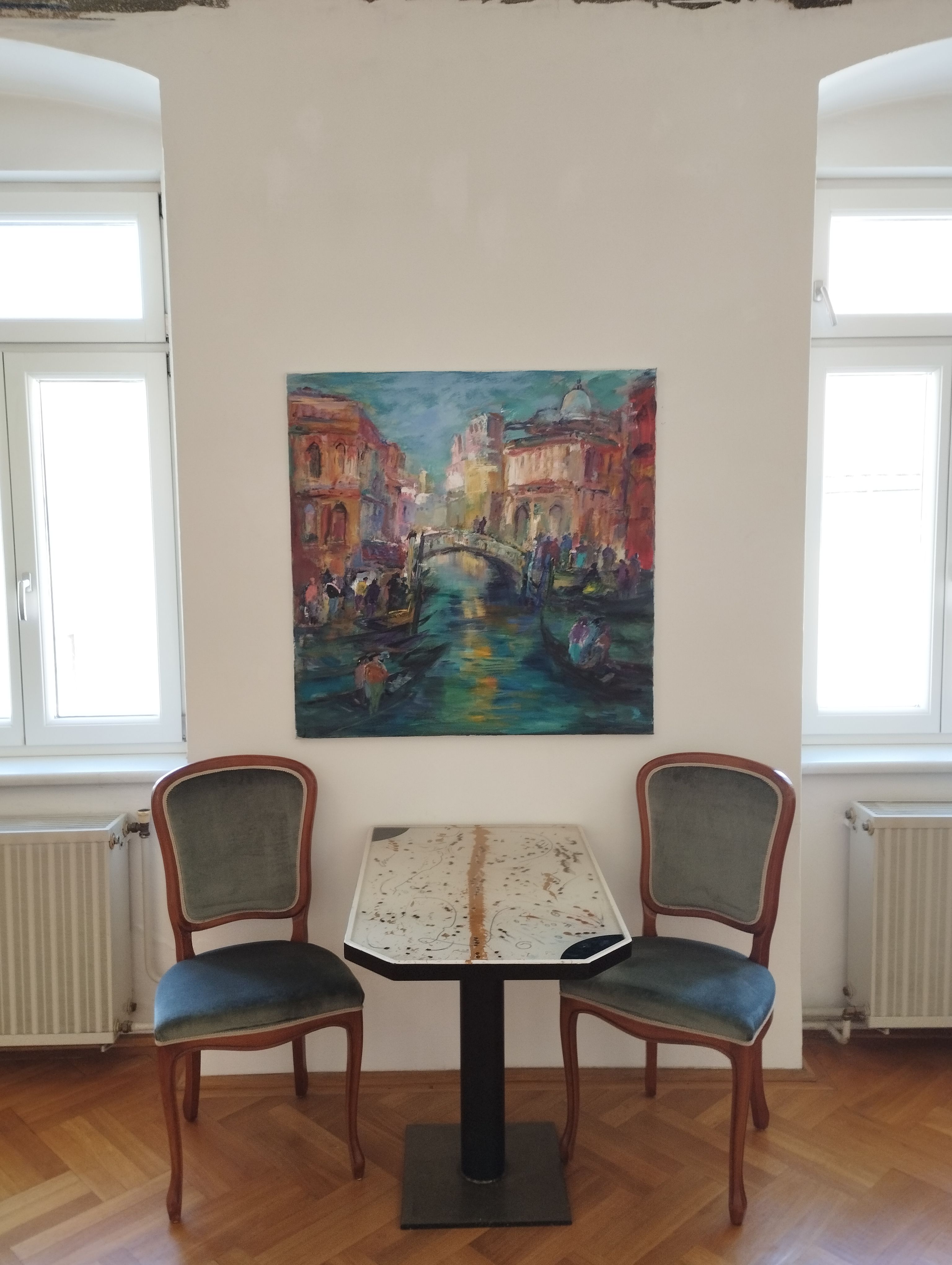 Zwei Stühle und ein Tisch vor einem Gemälde an einer weißen Wand.