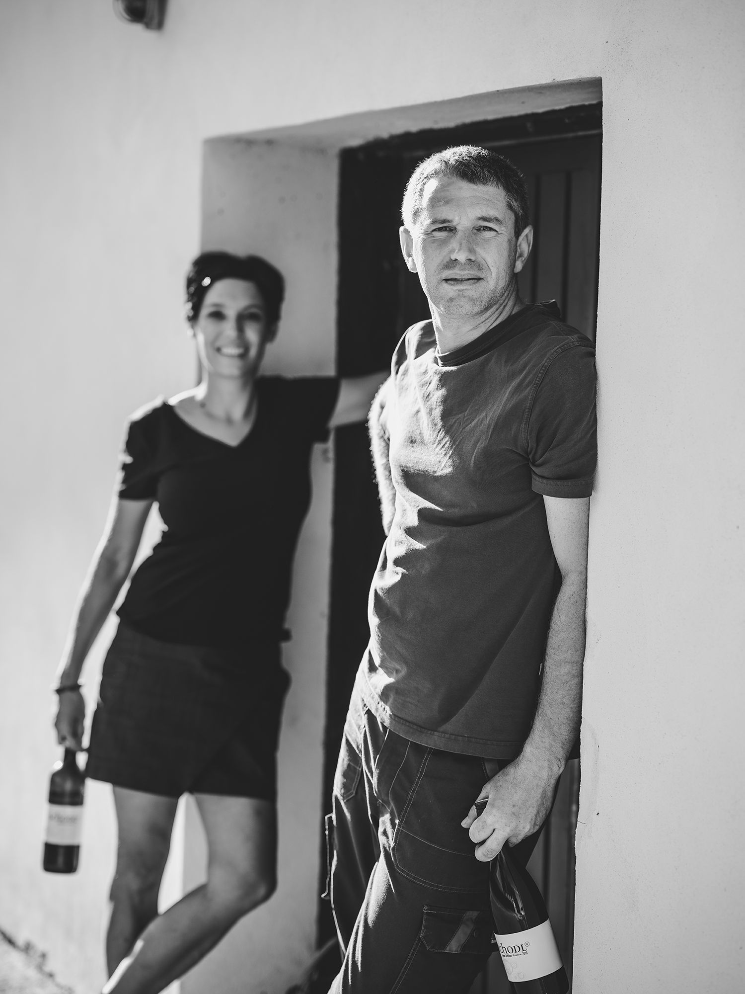 Black and white photo of two people with wine bottles in front of a door.