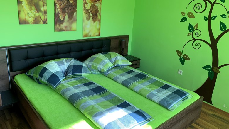 Schlafzimmer mit grünem Thema, Doppelbett, Wandbilder von Trauben und Baumdekoration.