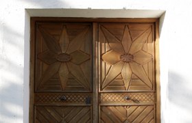 Holztür mit geometrischen Mustern in einer weißen Wand.