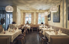 Elegantes Restaurant mit gedeckten Tischen, modernen Lampen und Kunst an den Wänden.