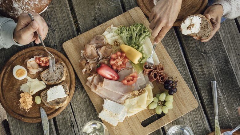 A rustic wooden table with a snack of bread, cheese, sausage, vegetables and wine.