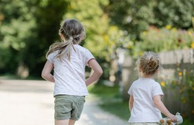 Zwei Kinder laufen auf einem Kiesweg in einem grünen Park.