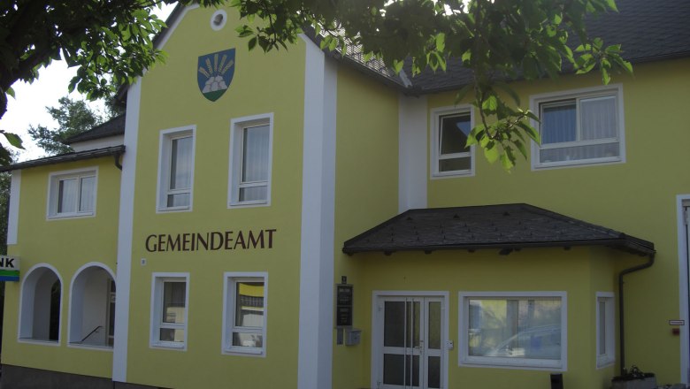 Gelbes Gebäude mit der Aufschrift 'GEMEINDEAMT' und einem Wappen darüber.
