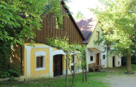 Traditionelle Weinkeller in der Kellergasse von Wolkersdorf, umgeben von grünen Bäumen und Weinreben.