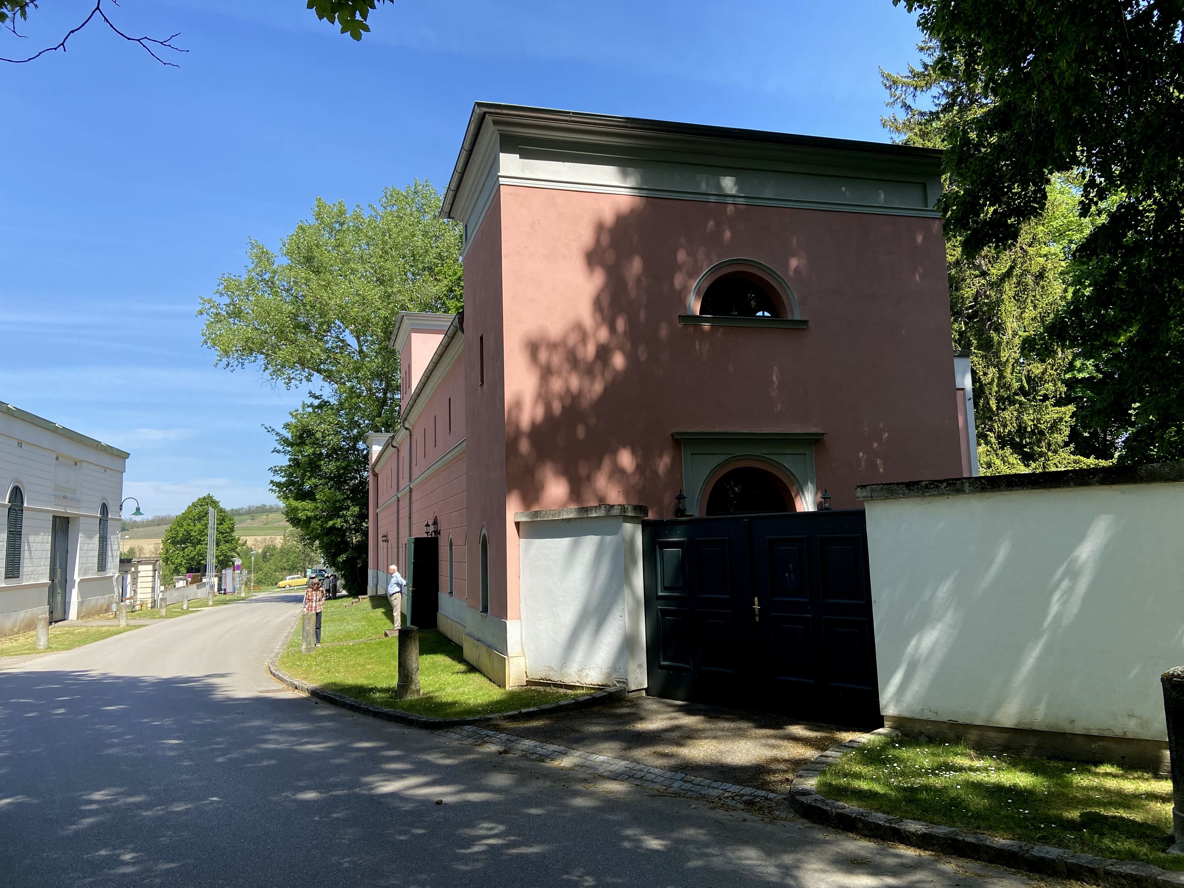 Straße mit rosa Gebäude und Bäumen bei sonnigem Wetter.