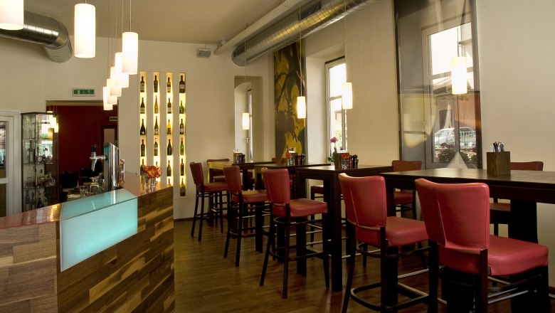 Innenansicht eines modernen Restaurants mit roten Stühlen und hölzernem Tresen.