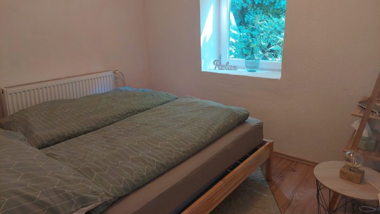 Ein gemütliches Schlafzimmer mit einem Bett, einem Fenster mit Blick ins Grüne und einem Bild an der Wand.