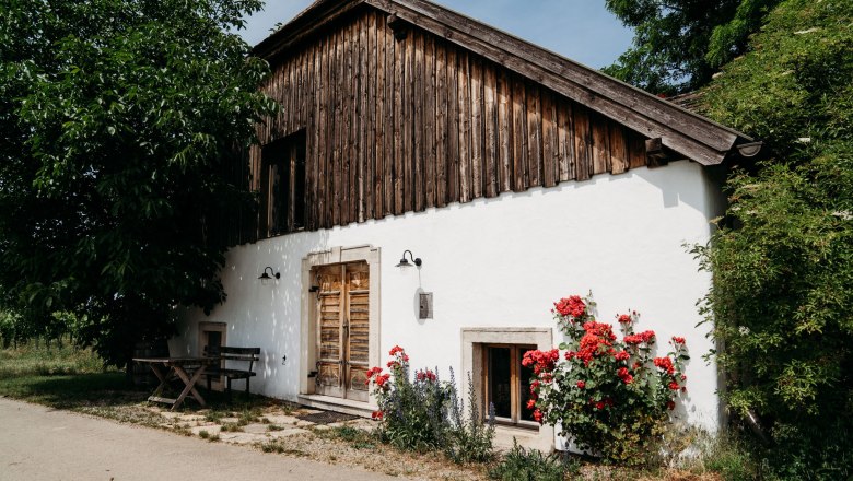 Außenansicht, © Weinakademie Retz Außenansicht eines Hauses mit Holzwänden, weißen Wänden und roten Blumen im Vordergrund.