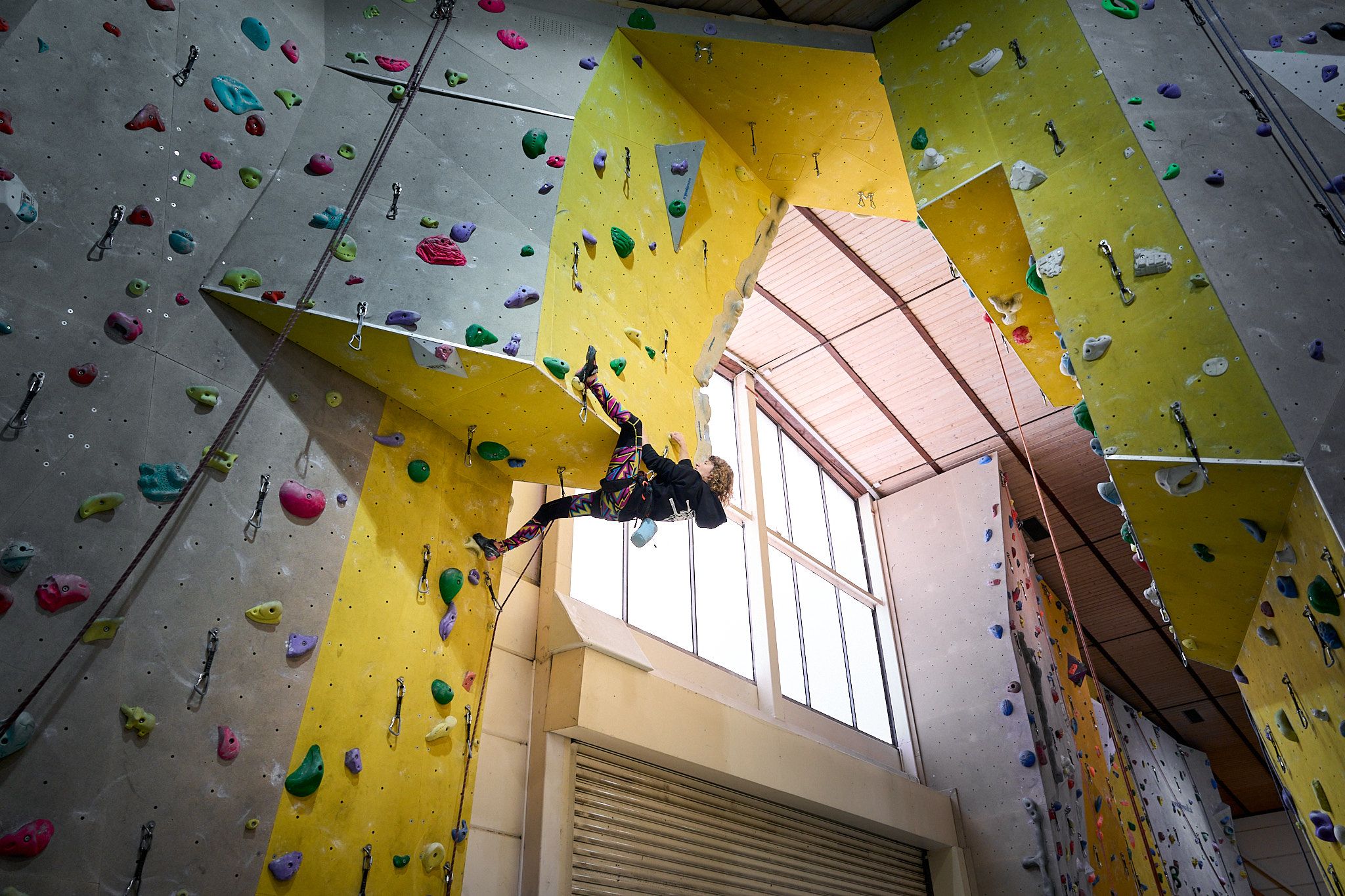 Person climbing on an indoor climbing wall with colorful holds.