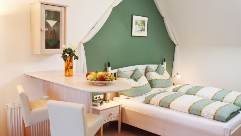 Gemütliches Schlafzimmer mit grün-weißer Bettwäsche, Holzmöbeln und Dekorationen.