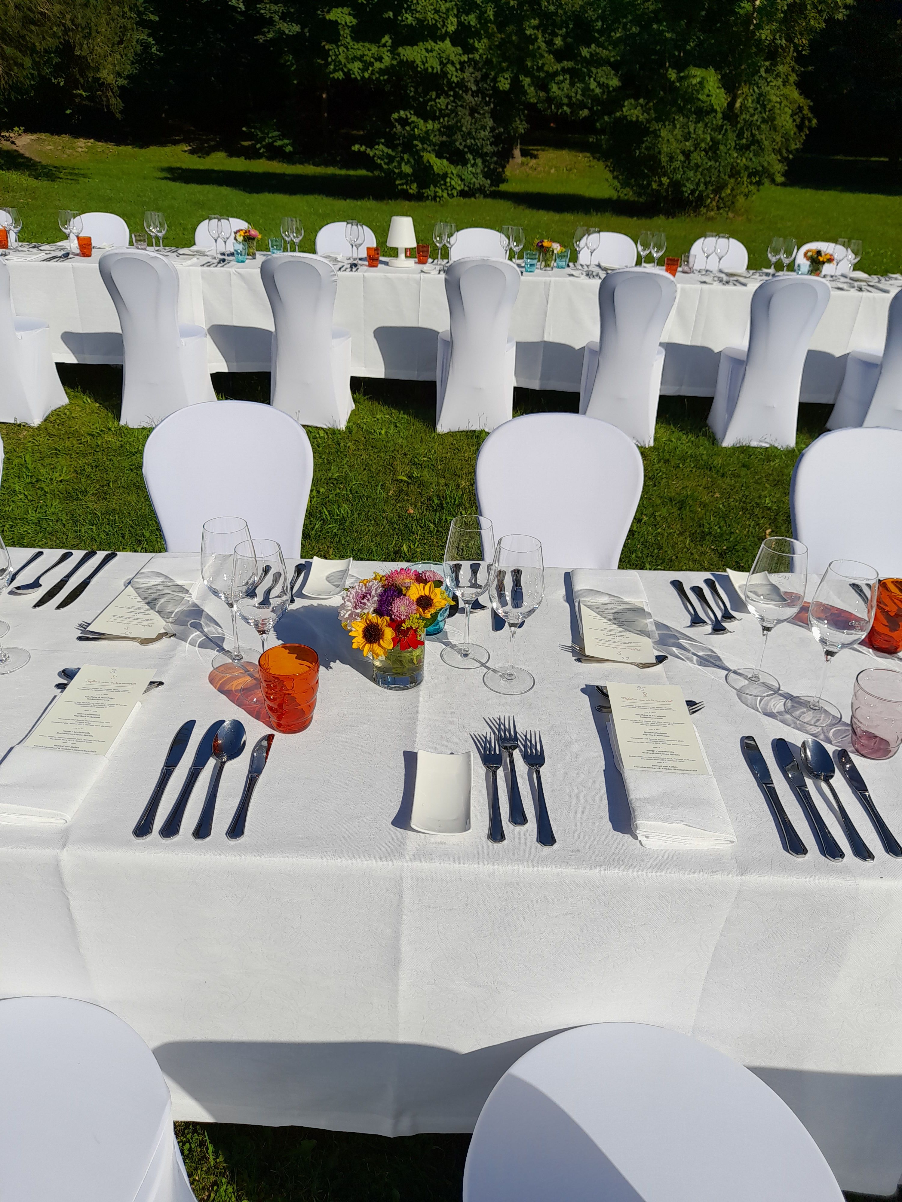 Festlich gedeckter Tisch im Freien mit weißen Tischdecken und Stuhlhussen.
