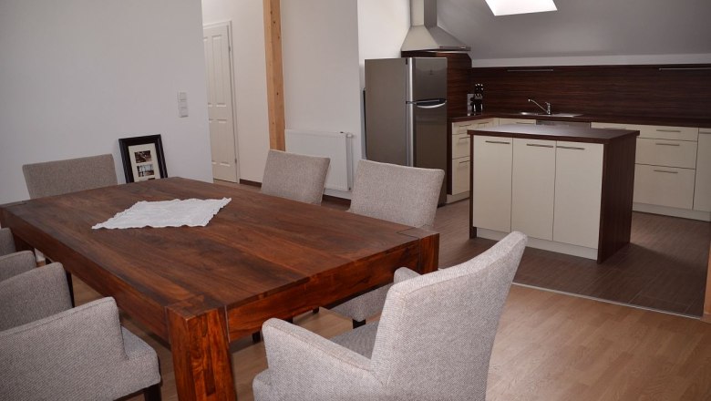 Moderner Essbereich mit Holztisch und grauen Stühlen, angrenzend an eine Küche mit Insel und Dachfenster.