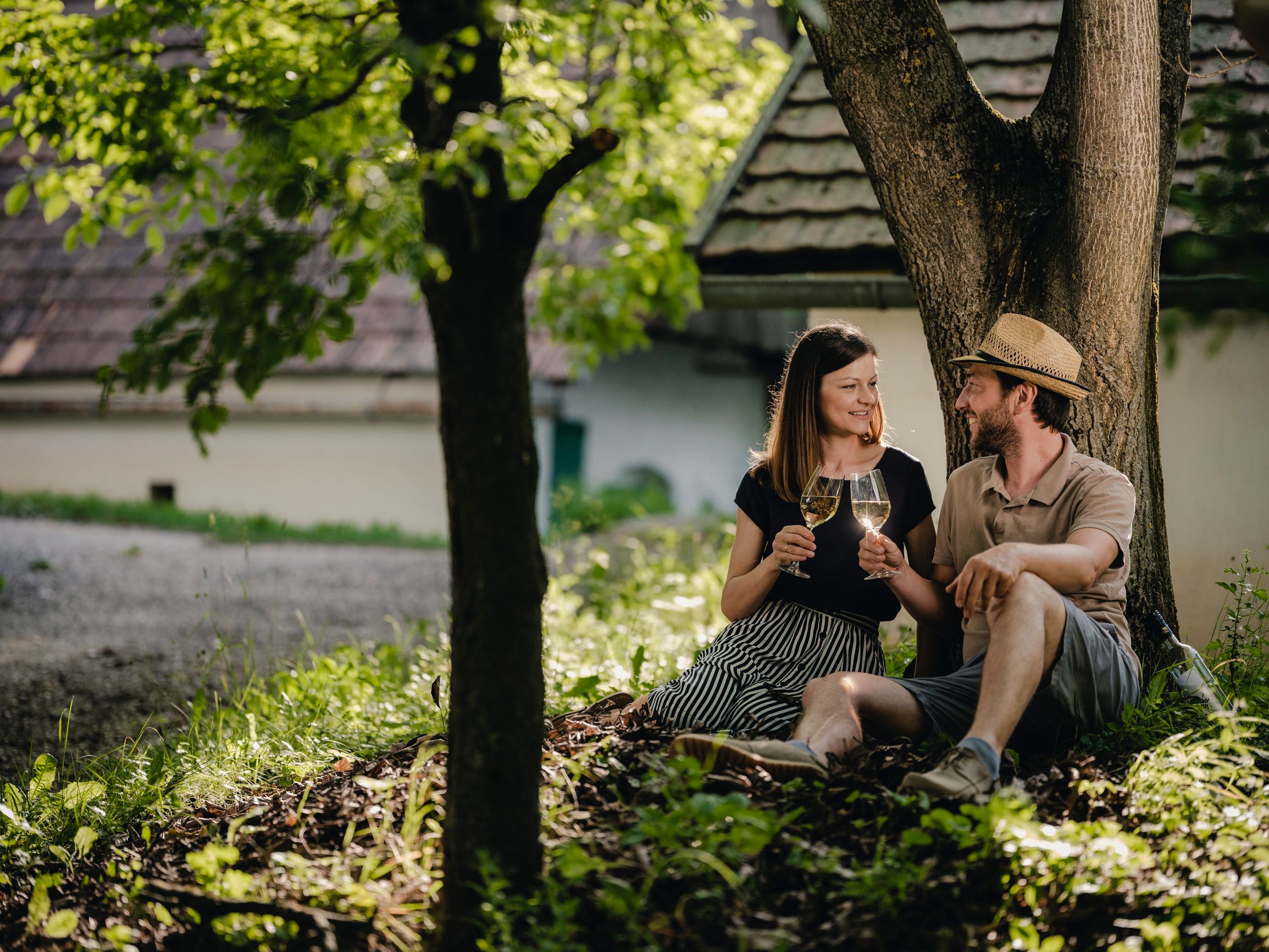 Ein Pärchen sitzt unter einem Baum und prostet sich mit Wein zu.