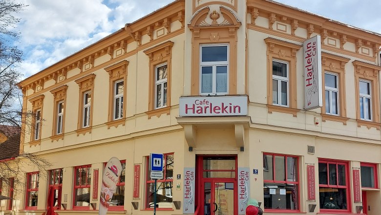 Außenansicht des Cafe Restaurant Harlekin mit gelber Fassade und roten Fenstern.