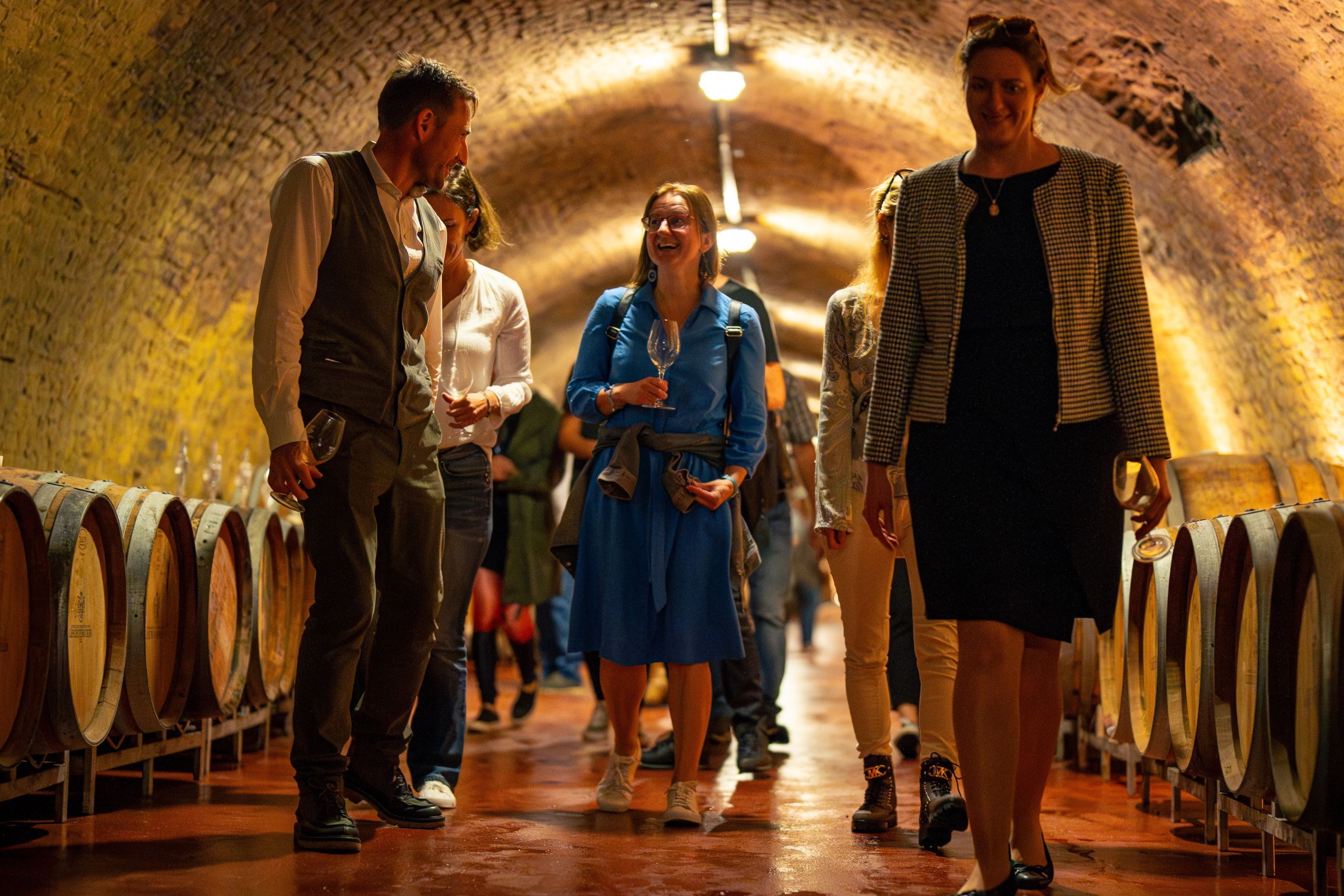 Eine Gruppe von Personen schlendert vorbei an Weinfässern durch einen Weinkeller.