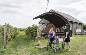 Eine Familie mit Fahrrädern vor einem Weingut mit großem Fass in Hohenruppersdorf.