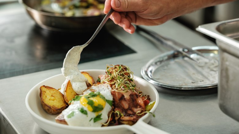 Ein Teller mit gebratenen Kartoffeln, Spiegelei und Sauce wird in einer K&uuml;che angerichtet.