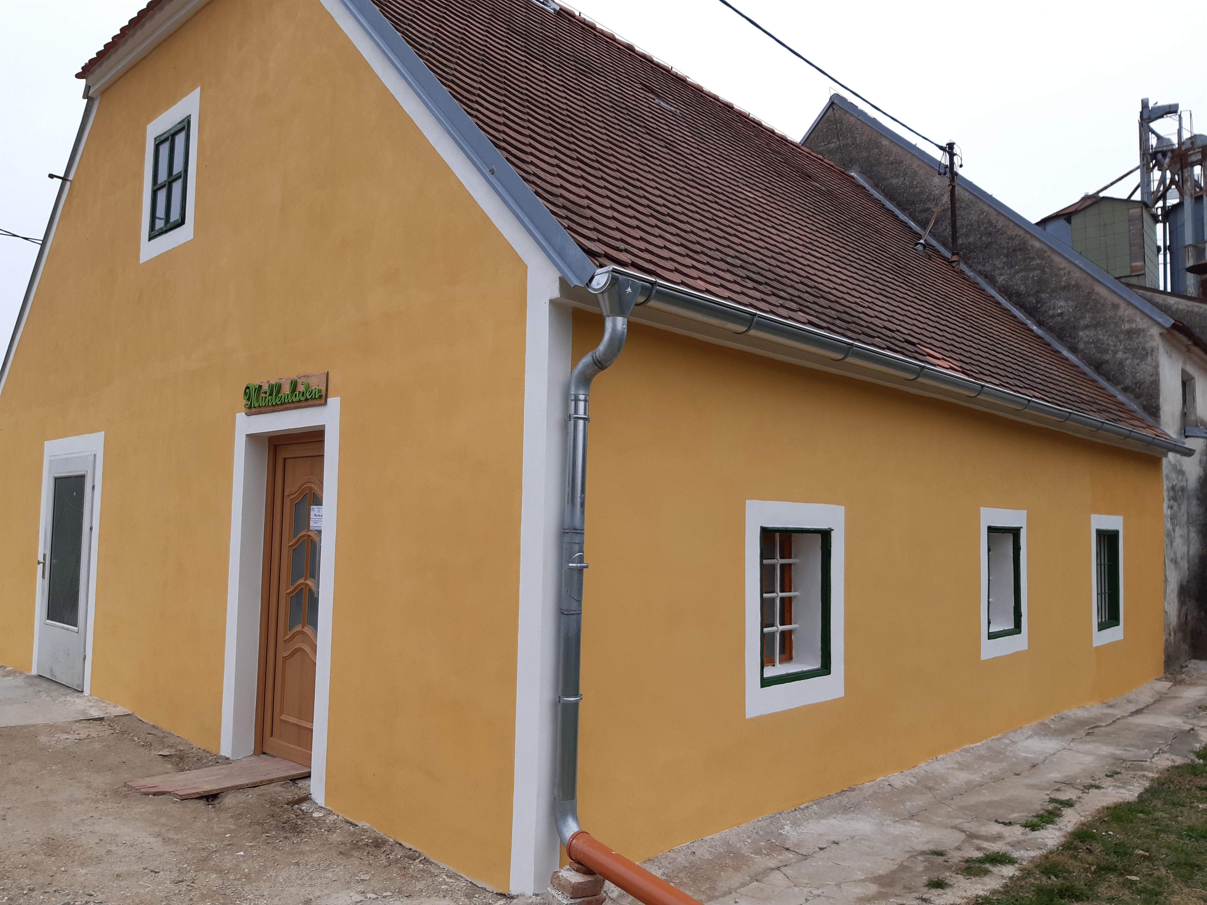 Gelbes Gebäude mit roten Dachziegeln und grünen Fensterrahmen, beschriftet mit 'Mühlenladen'.