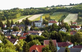 Landschaft mit Kirche und Dorf im Vordergrund, umgeben von Feldern und Hügeln.