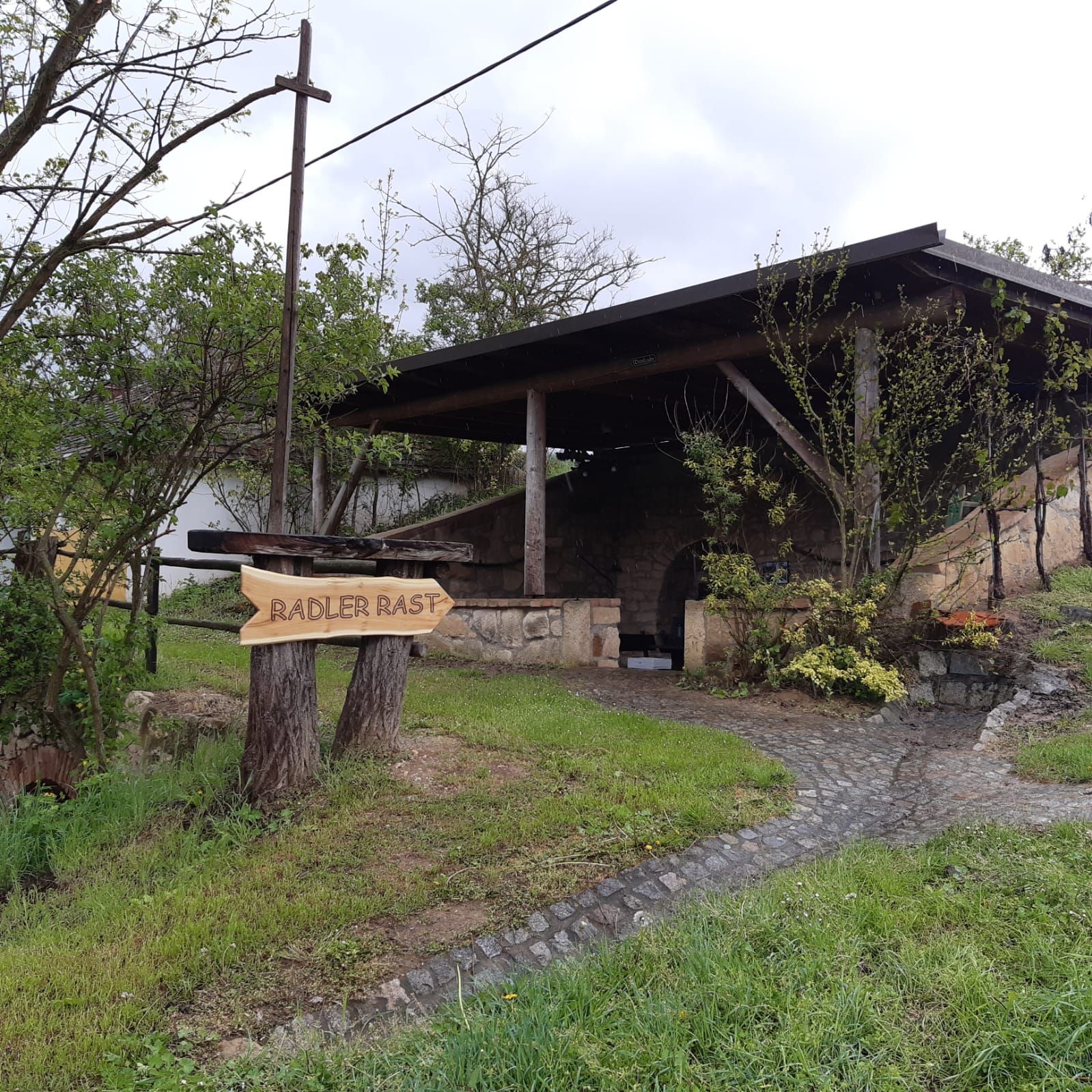 Ein Rastplatz für Radfahrer mit einem Holzschild, das "Radler Rast" anzeigt, und einem überdachten Bereich im Hintergrund.