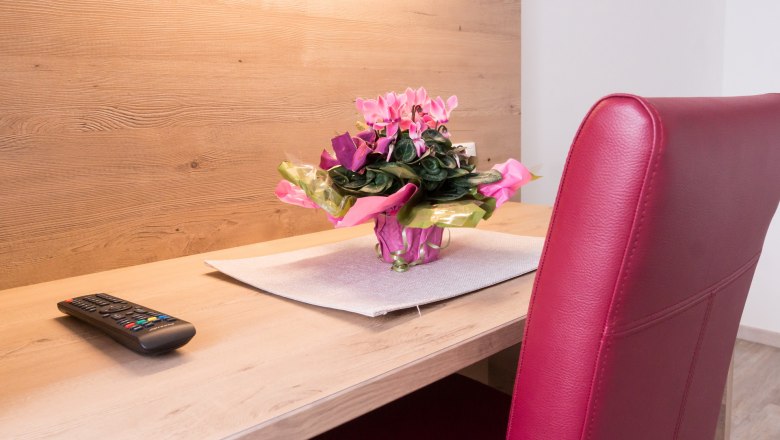 Ein Schreibtisch mit einer Fernbedienung, einem Blumenstrau&szlig; und einem roten Stuhl.