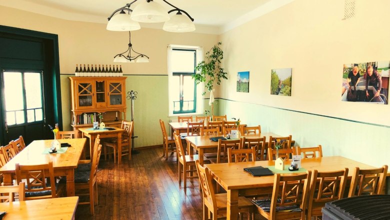 Ein gem&uuml;tlicher Gastraum mit Holztischen und -st&uuml;hlen, dekoriert mit Weinflaschen und Bildern an der Wand.