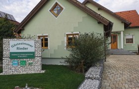 Grünes Haus mit Schild 'Gästezimmer Rieder' im Vorgarten.