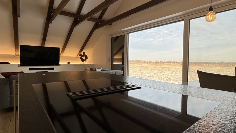 Moderner Wohn- und Essbereich mit Holzbalken, Kochinsel und großem Fenster mit Ausblick.