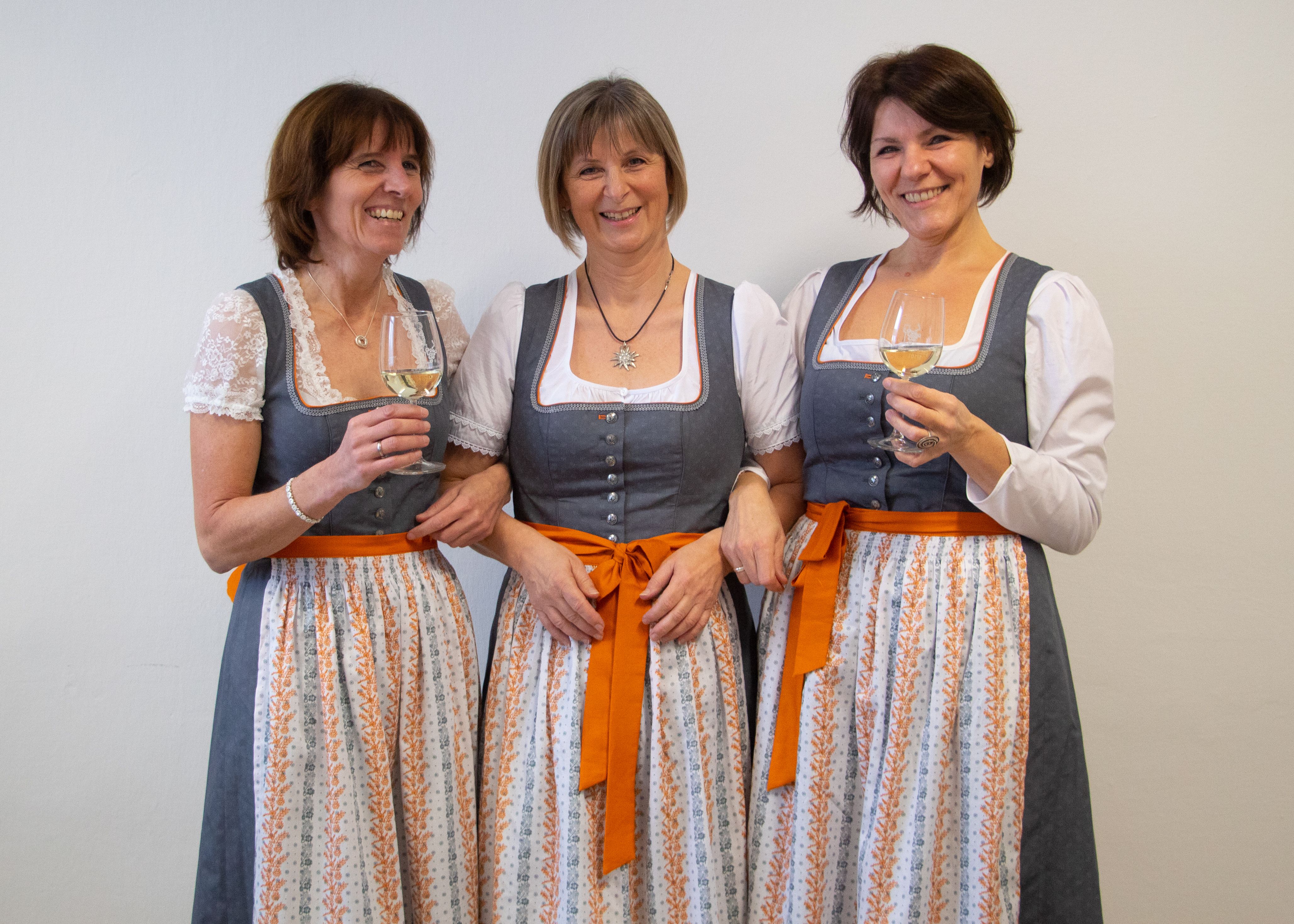 3 Frauen tragen ein Weinviertel-Dirndl in den Farben grau/orange, zwei der drei halten ein Glas Weißwein in der Hand.