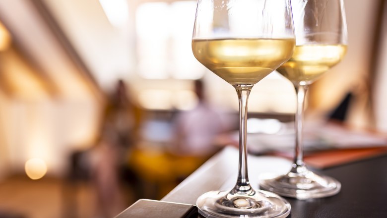 Zwei Gl&auml;ser Wei&szlig;wein auf einem Tisch, unscharfer Hintergrund.