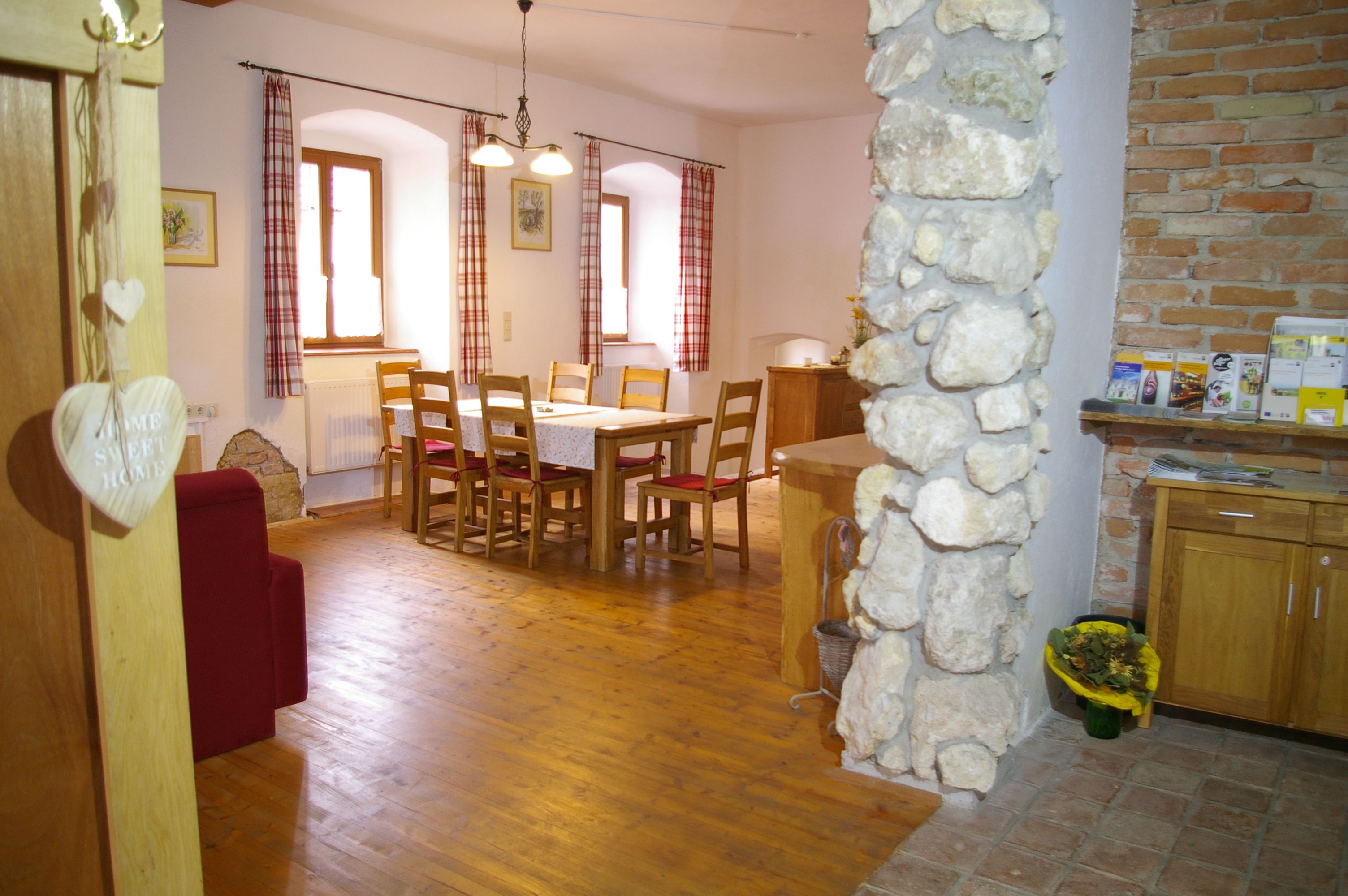 Cozy dining area with wooden table and chairs, red curtains and stone wall.