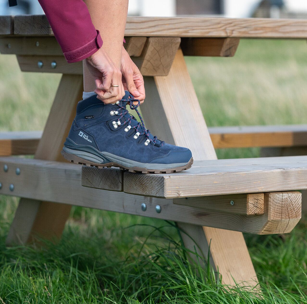 Eine Person hat den Fuß auf einer Holzbank abgestellt und schnürt den Wanderschuh zu.